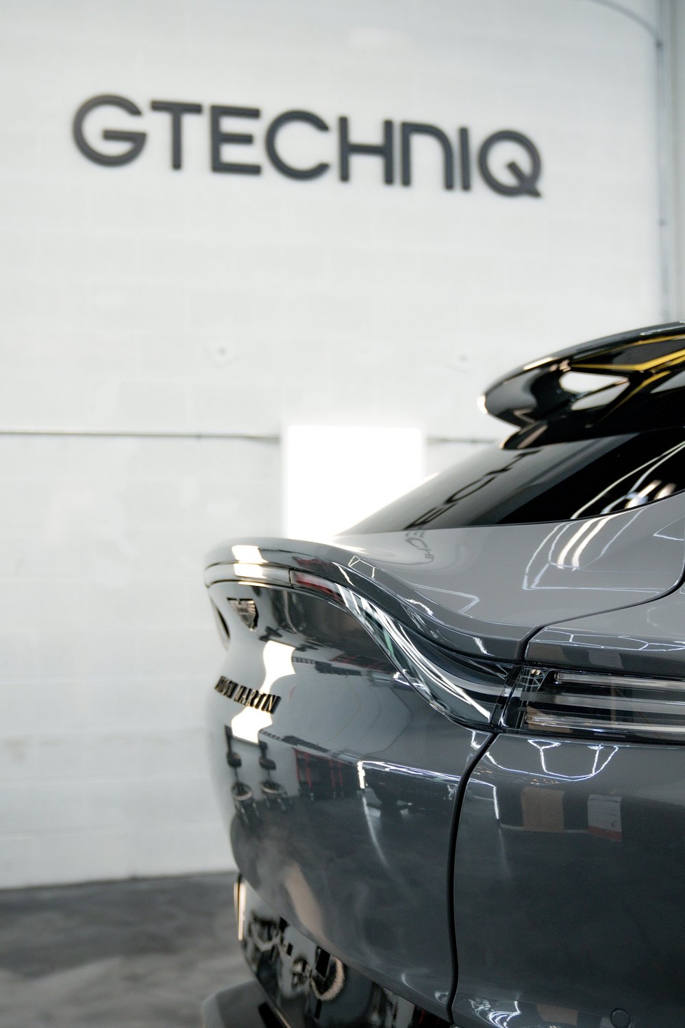 Rear view of a dark luxury car with the Gtechniq sign in the background